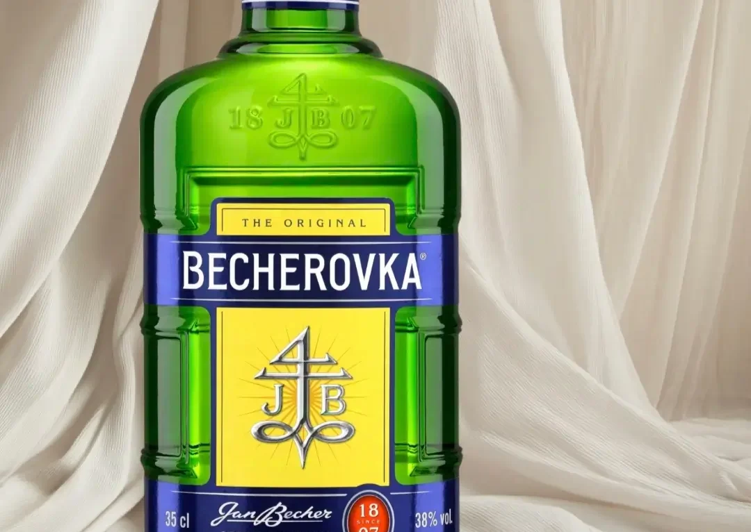 зеленый стеклянный флакон чешского травяного ликера Бехеровка на фоне драпированной светлой ткани